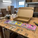 Aufkleber-Box Netter Held: 5 Aufkleber-Sets am Packtisch neben dem Versandkarton